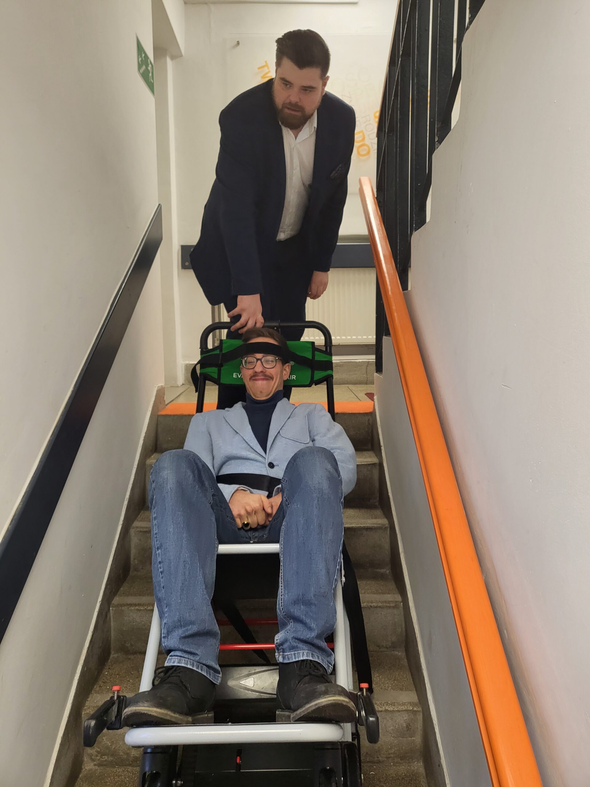 Pracownicy zjeżdżają wózkiem po schodach.