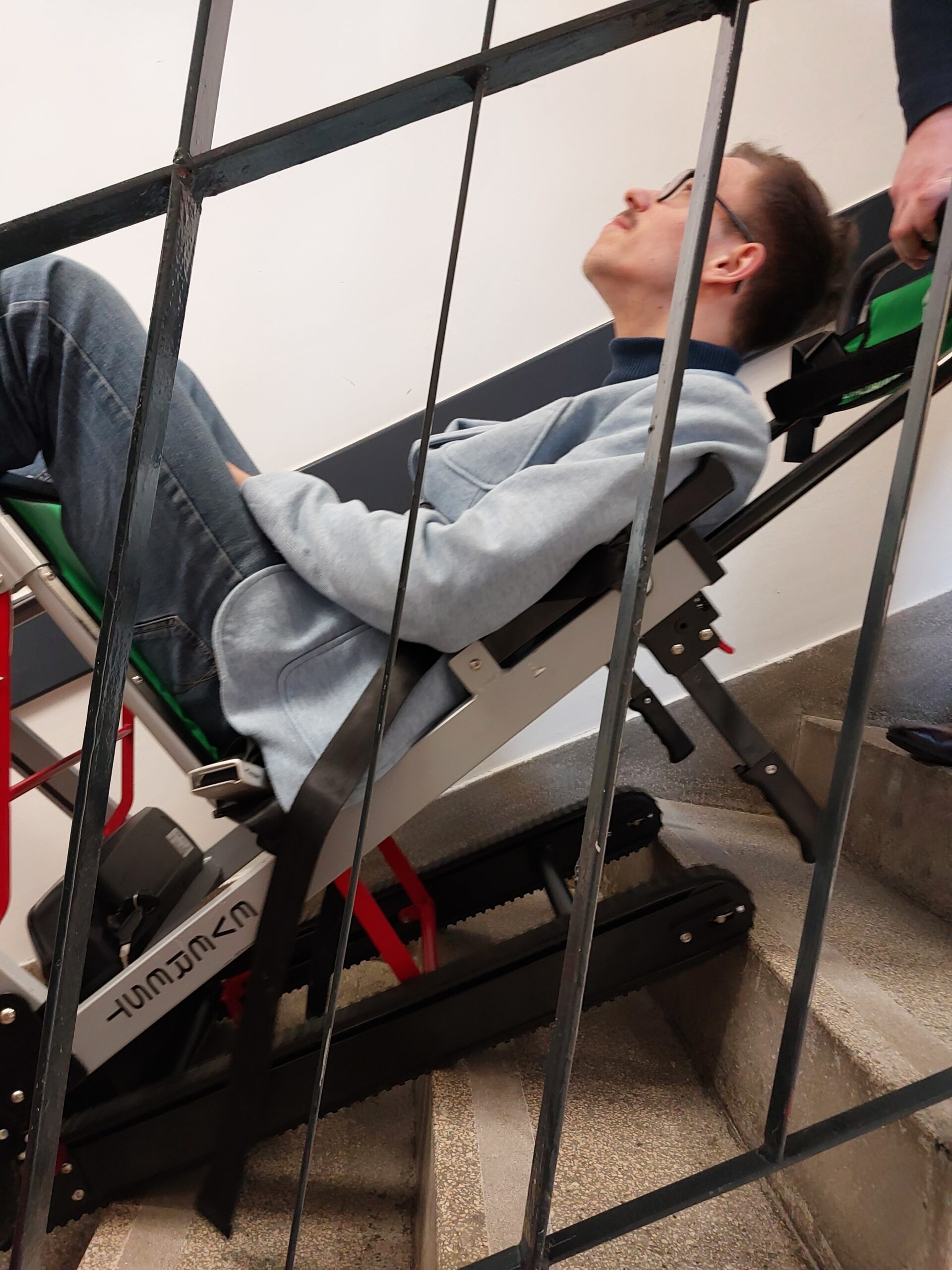 Pracownicy zjeżdżają wózkiem po schodach.