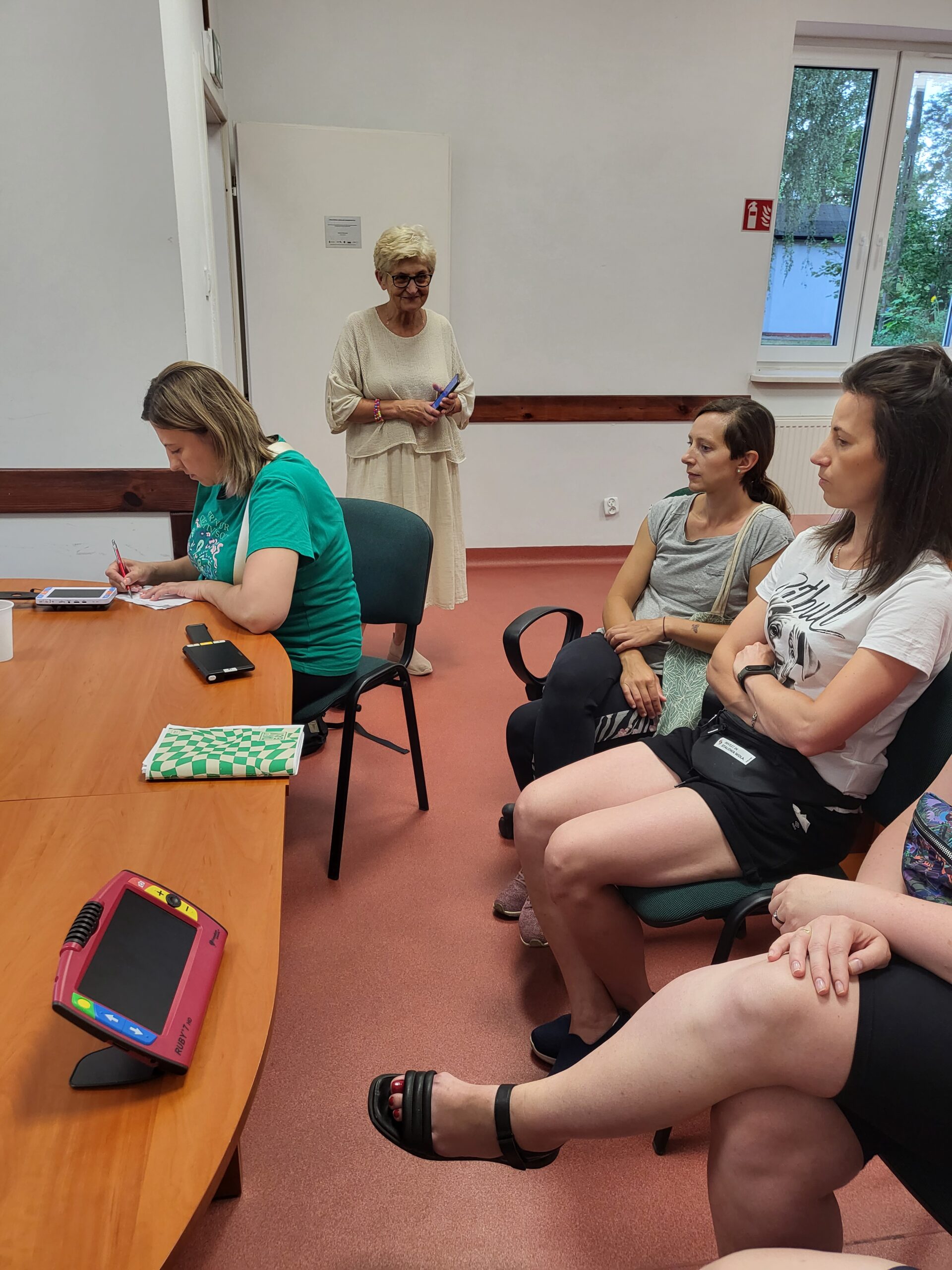 Uczestnicy oglądają różne sprzęty przy stole.