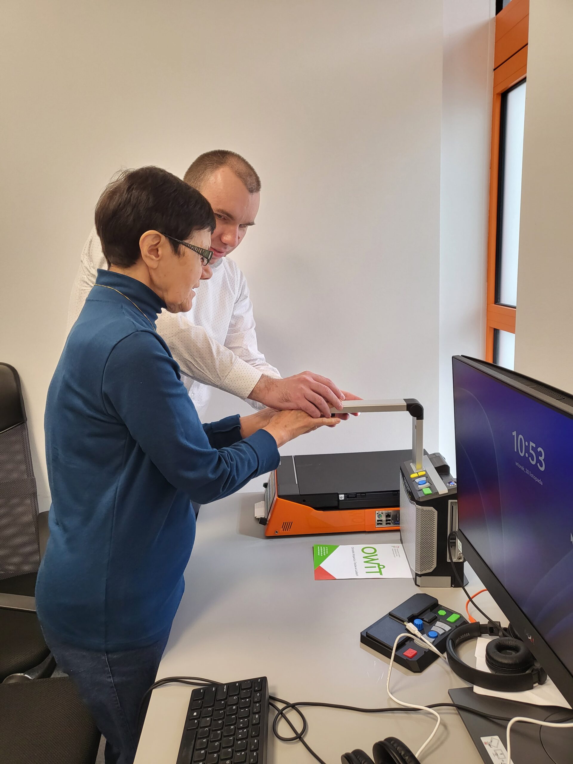 Pracownik pokazuje niewidomej osobie jedno z urządzeń.