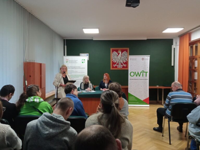 Pani Kierownik Działu ds. Absolwentów przemawia do mikrofonu, widok na scenę i banery OWiT i PFRON